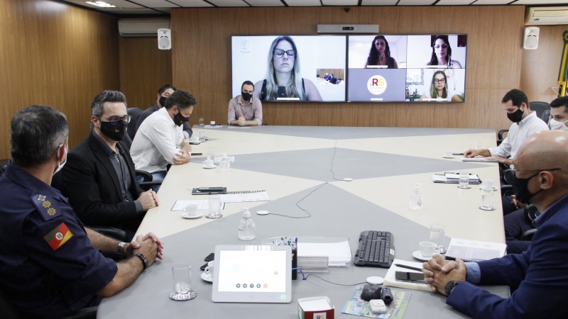 Imagem mostra os participantes da reunião presencialmente, em torno de uma mesa, e online