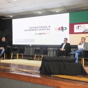 Três homens no palco diante de telão que exibe slide com o título "Estratégia & Governo Digital rs.gov.br" 